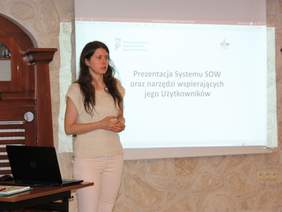 Pokaż zdjęcie: Magdalena Gursztyn specjalista ds. wdrożeń z Wydziału ds. projektu Systemu Obsługi Wsparcia finansowanego ze środków PFRON na tle ekranu multimedialnego