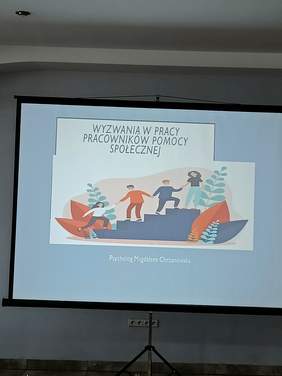 Pokaż zdjęcie: Na ekranie widnieje obrazek prezentacji zatytułowany: Wyzwania w pracy pracowników pomocy społecznej. Przedstawia grupę ludzi trzymających się za ręce. Każda z osób każdy stoi na innym schodku. 