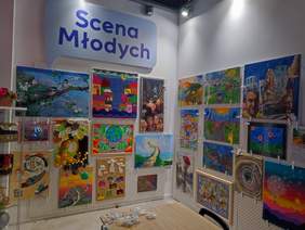 Pokaż zdjęcie: Na dwóch ścianach wyeksponowano dużą liczbę prac plastycznych, w róznych formatach i w różnych stylach, jest bardzo kolorowo.