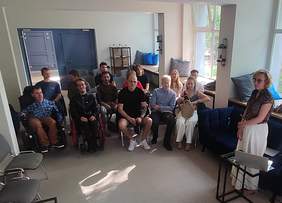 Pokaż zdjęcie: W niewielkiej sali w trzech rzędach siedzi grupa kilkunastu osób. Z przodu znajduje się kobieta, która prowadzi spotkanie i ma przed sobą laptop ustawiony na stoliku.