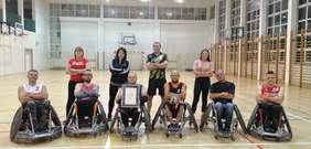 zawodnicy rzeszowskiej drużyny rugby, na sali gimnastycznej 6 mężczyzn na wózkach za nimi stoją 4 osoby - 3 kobiety i 1 mężczyzna