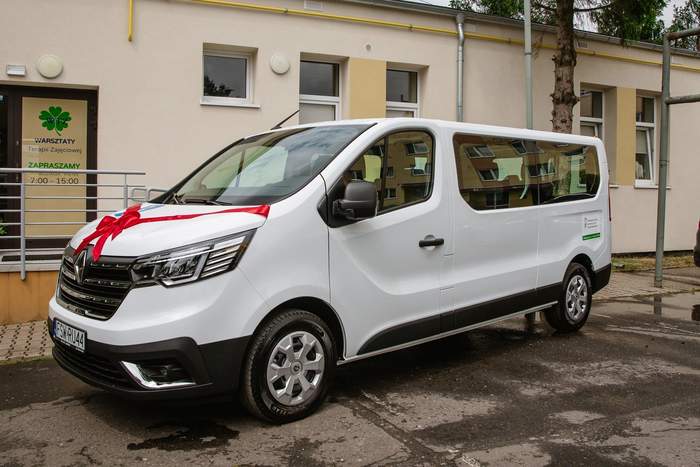 Pokaż zdjęcie: Biały bus w kokardą czerwoną na masce, stoi naprzeciwko fasady WTZ w Świebodzinie