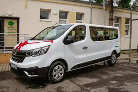 Pokaż zdjęcie: Biały bus w kokardą czerwoną na masce, stoi naprzeciwko fasady WTZ w Świebodzinie