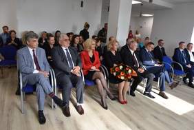 Pokaż zdjęcie: Na krzesłach w sali, na krzesłach w rzędach,  siedzą zaproszeni goście, w większości mężczyźni w garniturach.