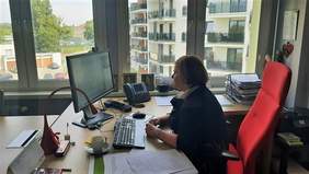 Dyrektor Kujawsko-Pomorskiego Oddziału PFRON siedzi na czarwonym krześle, przy biurku, podczas spotkania on line. Przed nią stoi monitor , na którym wyświetlany jest slajd prezentacji