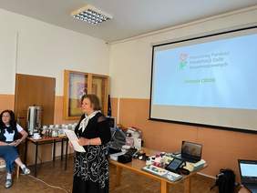 Spotkanie prowadzi Dyrektor Kujawsko-Pomorskiego Oddziału PFRON - Aleksandra Gierej. Za nią wisi ekran z wyświetlaną prezentacją.