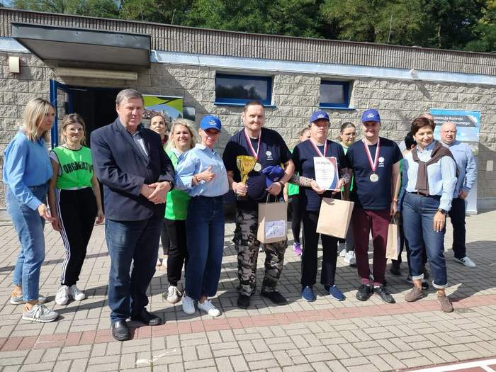 Pokaż zdjęcie: Grupa ponad dziesięciu osób pozuje do pamiątkowego zdjęcia, kilka osób trzyma w ręku dyplomy i torby z prezentami.