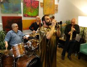 Pokaż zdjęcie: Zespół muzyczny. Na pierwszym planie muzyk gra na trąbce. 