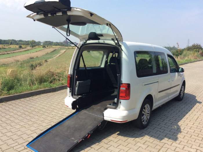 Pokaż zdjęcie: Widoczny samochód w kolorze białym, z otwartymi drzwiami tylnymi i rampą do wjazdu wózkiem