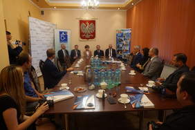 Pokaż zdjęcie: kilkanaście osób siedzi przy owalnym stole i dyskutuje