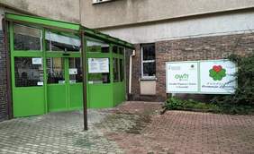 Pokaż zdjęcie: Główne wejście do ośrodka. Zilone, rozsuwane automatycznie drzwi. Po prawej stronie widzimy zielone logo OWiT na białym tle.