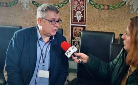 Pokaż zdjęcie: Pan Piotr Kopyciński, pracownik Oddziału Kujawsko-Pomorskiego PFRON udziela wywiadu dla Radia PiK, siedzi na krześle - ubrany w koszulę w paski i ciemną marynarkę, nosi okulary, po jego lewej stronie siedzi redaktorak, widoczna w połowie, trzyma czerwony mikrofon z logo radia