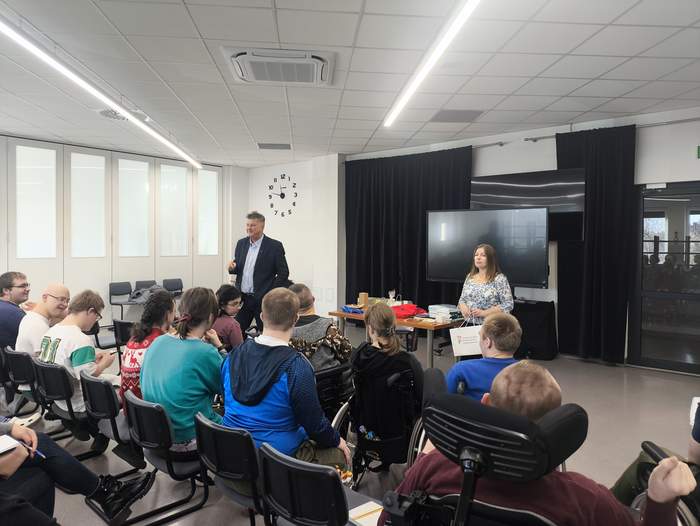 Pokaż zdjęcie: W sali zgromadziła się duża grupa młodzieży, w tym część osób na wózkach, przed młodzieżą stoi dwóch prelegentów.