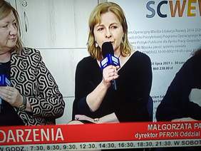 Pokaż zdjęcie: Na zdjęciu kobieta blondynka siedzi na krześle, trzyma w ręku mikrofon. 