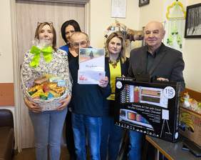 Pokaż zdjęcie: Do pamiątkowego zdjęcia pozuje pięć osób, jedna trzyma kosz cukierków, druga dyplom, kolejna zestaw plastyczny.