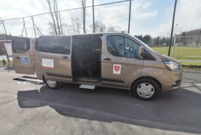 Pokaż zdjęcie: Pojazd dostosowany do przewozu osób z potrzebą wsparcia w zakresie mobilności zakupiony przez Gminę Iwanowice. Samochód widoczny z boku. Na pojeździe zamieszczone naklejki projektowe oraz oznaczenia.