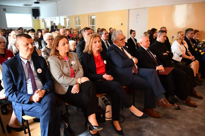 Pokaż zdjęcie: Zdjęcie zaproszonych osób siedzących na krzesełkach, elegancko ubranych.