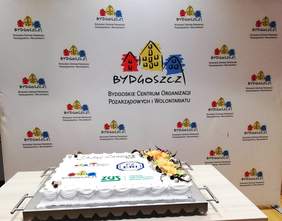 Tort z okazji Dnia Seniora, a w tle baner Bydgoskiego Centrum Organizacji Pozarządowych i Wolontariatu