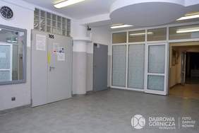 Pokaż zdjęcie: Fragment pomieszczenia w kolorach biało-szarych. Z prawej strony są duże przeszklone drzwi. Z lewej strony jest ściana z fragmentem dużego lustra i drzwiami. 