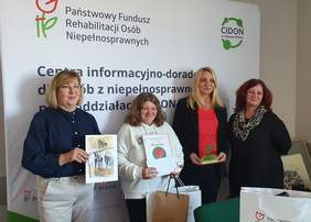 Pokaż zdjęcie: Cztery usmiechnięte kobiety na tle logotypów PFRON. Laureatka trzyma nagrody.