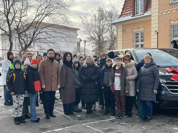 Pokaż zdjęcie: Obok auta przed budynkiem stoją uczniowie SOSW w Międzyrzeczu wraz z osobami biroącymi udział w uroczystości przekazania busa