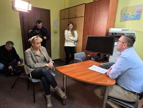 Pokaż zdjęcie: W pokoju znajduje się pięć osób: dwie kobiety i jeden mężczyzna. Trwa nagrywanie odcinka programu pt. "Nie poddaję się". Widać kamerę filmową, która nagrywa wypowiedź jednego pana. 