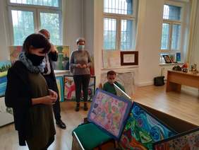 Pokaż zdjęcie: 2 kobiety i 2 mężczyzn ogląda prace plastyczne ustawione w dużym pomieszczeniu