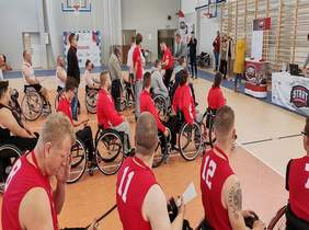 Pokaż zdjęcie: na zdjęciu hala sportowa w której zawodnicy drużyn sportowych na wózkach otrzymują od organizatora medale oraz puchary  