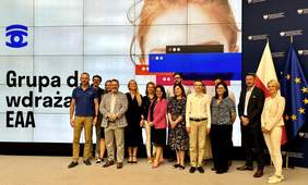 Pokaż zdjęcie: Członkowie Grupy roboczej do spraw wdrażania EAA. Siedmiu mężczyzn i osiem kobiet. W tle biała ścianka z głową kobiety i napisem Grupa do wdrażania EAA.
