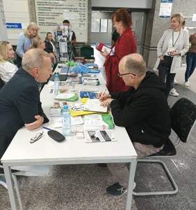 Pokaż zdjęcie: Rozmowa z doradca CIDON przy białym stole z kolorowymi ulotkami