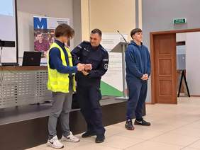 Policjant i dwóch słuchaczy podczas prelekcji stoją na środku sali