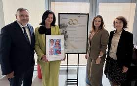 Trzy kobiety i jeden mężczyzna pozują do zdjęcia. Pomiędzy nimi stoi plakat z informacją o jubileuszu.