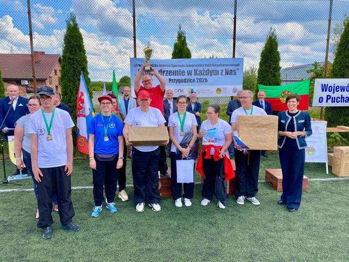 Pokaż zdjęcie: Grupa kilkunastu osób stoi na boisku. Wśród nich są przedstawiciele instytucji i zawodnicy z otrzymanymi medalami.