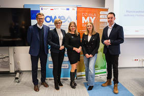 Pokaż zdjęcie: Grupa pięciu osób stoi wspólnie przed roll-upami promującymi projekt „DziałaMY Razem” oraz Ośrodek Wsparcia Ekonomii Społecznej podczas spotkania informacyjnego w Białymstoku.