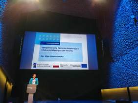 Kobieta za mównicą, w zielonej marynarce