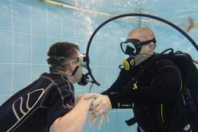 Na zdjęciu dwóch mężczyzn zanurzonych w basenie. Ubrani w kombinezony piankowe, maski i aparaty tlenowe do nurkowaniaw k