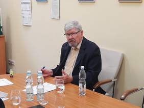 Pokaż zdjęcie: Przy biurku siedzi dyrektor Łódzkiego Oddziału PFRON. Trzyma w dłoni długopis. Przed nim leży umowa do podpisu. 