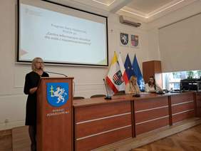 Pokaż zdjęcie: Od lewej na zdjęciu Wicestarosta Powiatu Jędrzejowskiego, dwie pracownice Oddziału Świętokrzyskiego PFRON, w tle prezentacja wyświetlana przez rzutnik