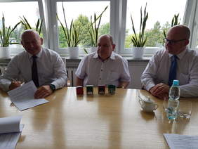 trzech mężczyzn w białych koszulach siedzą w rzędzie przy stole nad dokumentami