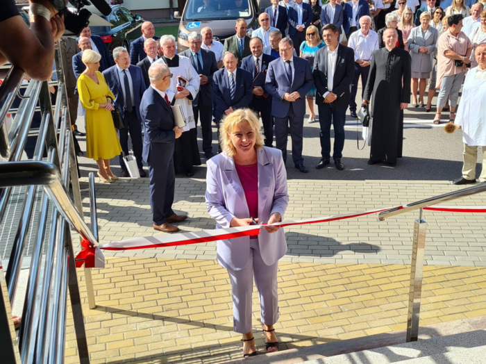 Pokaż zdjęcie: Kobieta blondynka w liliowym garniturze przecina wstęgę