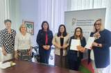 Przy stole konferencyjnym sześć osób pozuje do zdjęcia podczas podpisania umów z PFRON. Dwie osoby trzymają dokumenty, w tle widoczny jest roll-up Funduszu.