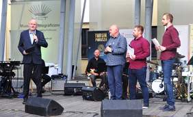 Pokaż zdjęcie: Prezydent Miasta Torunia - Michał Zaleski - wita uczstników Festiwalu, obok niego na scenie stoją Pan Mirosław Satora oraz prowadzący koncert