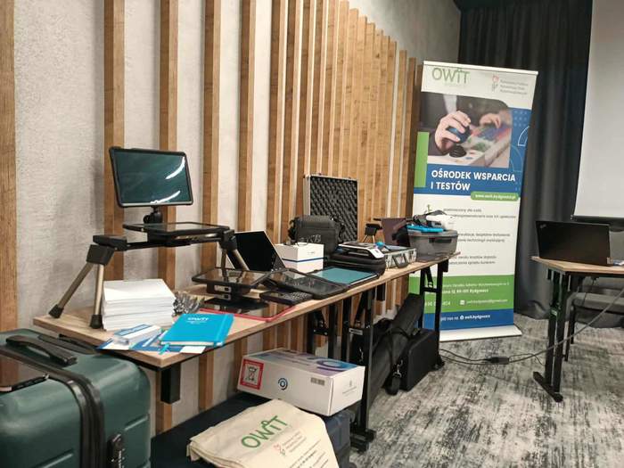 Nowoczesne technologie dla osób niepełnosprawnych, leżą na stole, w tle baner Ośrodka Wsparcia i Testów