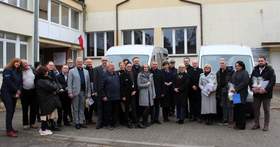 Zdjęcie grupowe wykonane na zewnątrz przed budynkiem. Na zdjęciu widać kilkanaście osób stojących w jednym rzędzie, ubrane w płaszcze i kurtki. W tle stoją dwa srebrne busy dla Warsztatów Terapii Zajęciowej w Grodzisku Wielkopolskim i Rakoniewicach.