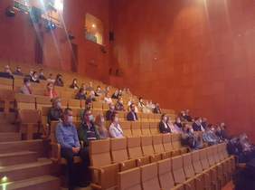 Pokaż zdjęcie: na zdjęciu sala koncertowa, osoby siedzą na widowni w maseczkach oddzieleni od siebie, oglądają występ artystyczny