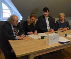 Pokaż zdjęcie: Przy stole siedzi dwóch mężczyzn i dwie kobiety, podpisują dokumenty