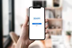 telefon kmórkowy, trzymany w dłoni, z uruchomioną aplikacją ZOOM na ekranie 