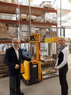 Pokaż zdjęcie: Dwie osoby w hali magazynowej, w tlewózek widłowy i regały