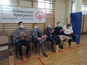 Pokaż zdjęcie: mężczyźni ubrani w stylu biznes casual siedzą na krzesełkach w trybunie honorowej