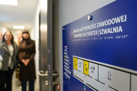 Tablica informacyjna na niebieskim tle z tekstem "ZAKŁAD AKTYWNOŚCI ZAWODOWEJ BUDYNEK B4 PARTER